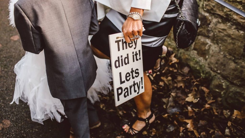 A woman holding a sign at a wedding that says "They did it Let's party!"